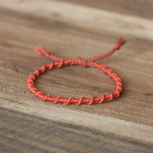 Op de afbeelding: Een rood gevlochten armbandje op een houten oppervlak.