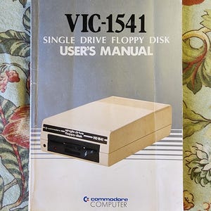 May include: A vintage Commodore VIC-1541 single drive floppy disk user's manual. The cover features a photo of the VIC-1541 drive and the Commodore logo.