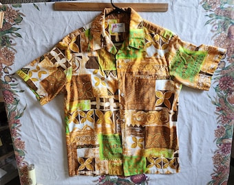 Op de afbeelding: Een kort mouw overhemd met knopen en een geometrisch patroon in bruin, groen en wit. Het overhemd heeft een kraag en een knoopsluiting. Het label op het overhemd luidt "Made in Hawaii".