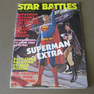 May include: A magazine cover featuring Superman and a character from the TV show Battlestar Galactica. The cover text reads "Star Battles" and "Superman Extra".