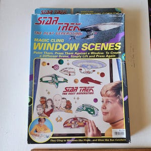 May include: A box of Star Trek: The Next Generation Magic Cling Window Scenes. The box features a colorful image of the Enterprise-D, characters from the show, and a child looking at the window scenes. The text on the box reads "Magic Cling Window Scenes" and "Paint Them. Press Them Against a Window. To Create a Different Scene, Simply Lift and Press Again."