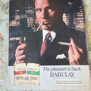 May include: Vintage advertisement for Barclay cigarettes. The image features a man in a suit holding a lit cigarette and a lighter. Two packs of Barclay cigarettes are displayed, with the text "99% tar free." The tagline reads, "The pleasure is back."