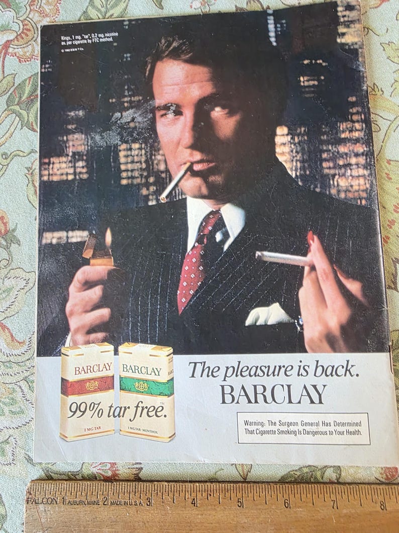 May include: Vintage advertisement for Barclay cigarettes. The image features a man in a suit holding a lit cigarette and a lighter. Two packs of Barclay cigarettes are displayed, with the text "99% tar free." The tagline reads, "The pleasure is back."