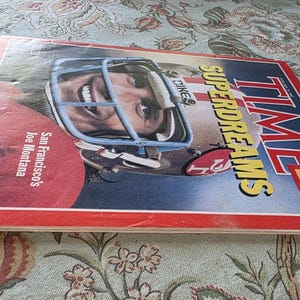 May include: A vintage TIME magazine cover featuring San Francisco's Joe Montana. The cover has a red border with the TIME logo and the headline "SUPERDREAMS." The image shows a football player in a helmet.
