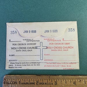 May include: Vintage Holy Cross Church offering envelopes from January 9, 1938, with a cross graphic. The envelopes have spaces for weekly offerings and include text about church support and debt. A wooden ruler is at the bottom.