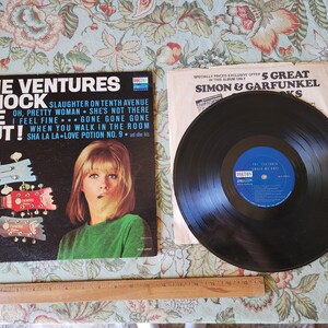 May include: A black vinyl record with a black and white album cover featuring The Ventures band. The album cover has the title "Knock Me Out!" and lists songs like "Slaughter on Tenth Avenue", "Oh, Pretty Woman", "She's Not There", "I Feel Fine", "Gone Gone Gone", "When You Walk in the Room", and "Sha La La Love Potion No. 9".
