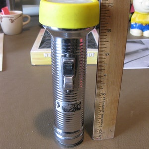 May include: A silver flashlight with a yellow plastic cap and a black switch. The flashlight is about 7 inches long and has the words "SKABERC USA" printed on the side.