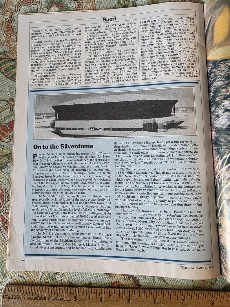 May include: A black and white photograph from Time Magazine, January 25, 1982, featuring the Silverdome stadium. The stadium is a large, enclosed structure with a distinctive roof, set against a backdrop of text.