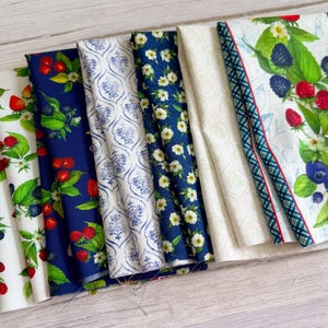 Può includere: Una collezione di sei campioni di tessuto piegati con vari motivi, tra cui fragole rosse su bianco, bacche rosse su blu navy, una stampa damascata blu e bianca, fiori bianchi su blu navy, un crema tinta unita e una stampa con bacche e foglie.