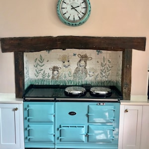 May include: A light blue AGA range cooker with four ovens and two hotplates. The cooker is set against a tiled backsplash featuring a whimsical design of cows and butterflies.