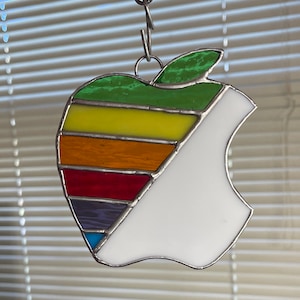 May include: A stained glass rainbow apple ornament with a white background. The apple is made of different colored glass pieces, including green, yellow, orange, red, purple, and blue.