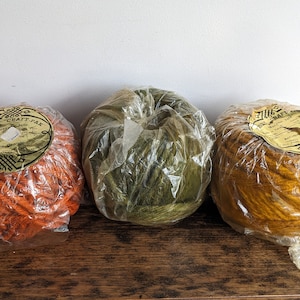 May include: Three balls of yarn in orange, green, and yellow, wrapped in clear plastic. Each ball has a label with the text "Strand Craft Pak" and a design.