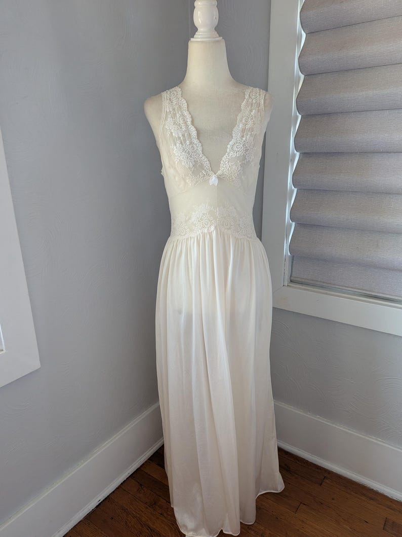 May include: Ivory-colored, sleeveless nightgown with a V-neckline. The bodice and neckline are adorned with delicate white lace. The flowing skirt drapes to the floor. The nightgown is displayed on a mannequin.