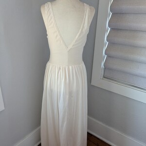 May include: Cream-colored vintage nightgown on a mannequin. The gown features a V-neckline with lace trim and a flowing, floor-length skirt. The fabric appears to be a soft, silky material. The back of the gown is visible, showcasing the delicate design.