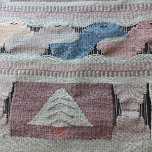 Pode incluir: Uma tape&ccedil;aria de parede tecida com um esquema de cores rosa, verde e azul. O design apresenta uma &aacute;rvore estilizada, nuvens e p&aacute;ssaros. A tape&ccedil;aria tem uma borda de franjas.