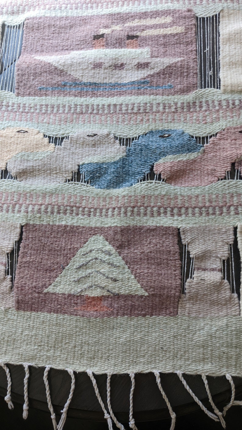 Pode incluir: Uma tape&ccedil;aria de parede tecida com um esquema de cores rosa, verde e azul. O design apresenta uma &aacute;rvore estilizada, nuvens e p&aacute;ssaros. A tape&ccedil;aria tem uma borda de franjas.