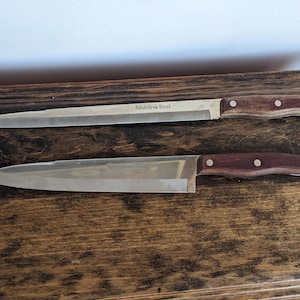 Puede incluir: Dos cuchillos de cocina de acero inoxidable con mangos de madera marrón. El cuchillo superior tiene el texto "Solingen Steel" en la hoja. El cuchillo inferior tiene el texto "Solingen 3404" en la hoja.