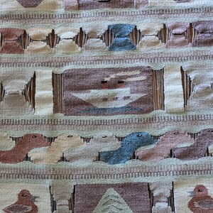 Pode incluir: Uma tape&ccedil;aria de parede tecida com um design geom&eacute;trico que apresenta p&aacute;ssaros, &aacute;rvores e vasos estilizados. A tape&ccedil;aria &eacute; feita de um tecido bege e marrom com uma borda de franjas.