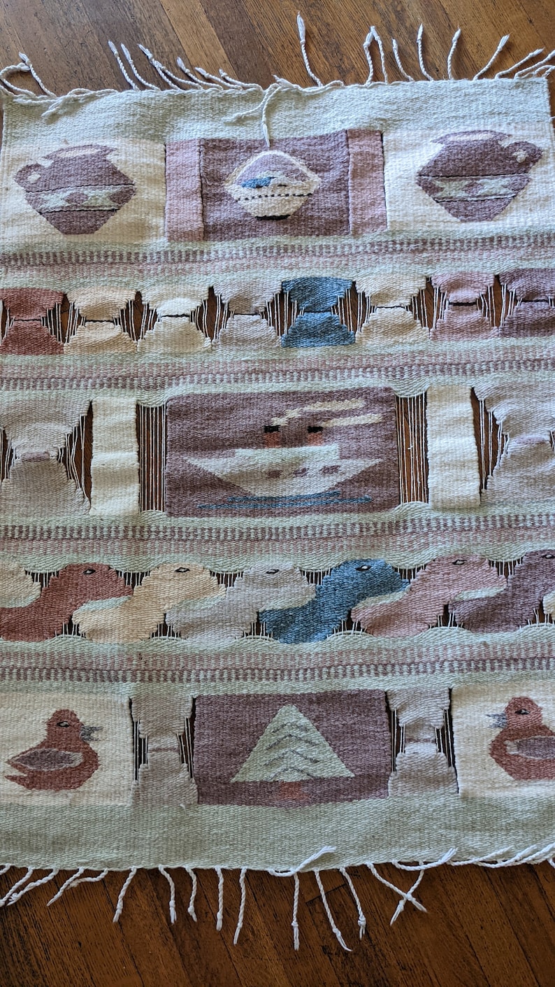 Pode incluir: Uma tape&ccedil;aria de parede tecida com um design geom&eacute;trico que apresenta p&aacute;ssaros, &aacute;rvores e vasos estilizados. A tape&ccedil;aria &eacute; feita de um tecido bege e marrom com uma borda de franjas.