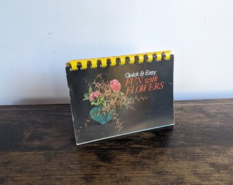 May include: A vintage book titled "Quick & Easy Fun with Flowers" with a yellow spiral binding. The cover features a photo of a bouquet of pink flowers in a blue vase.