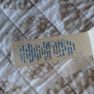 May include: A close-up of a tag with the text "RODICE" and fabric composition details: 50% nylon, 10% spandex, and 100% nylon skirt. The tag also includes washing instructions and "MADE IN U.S.A."