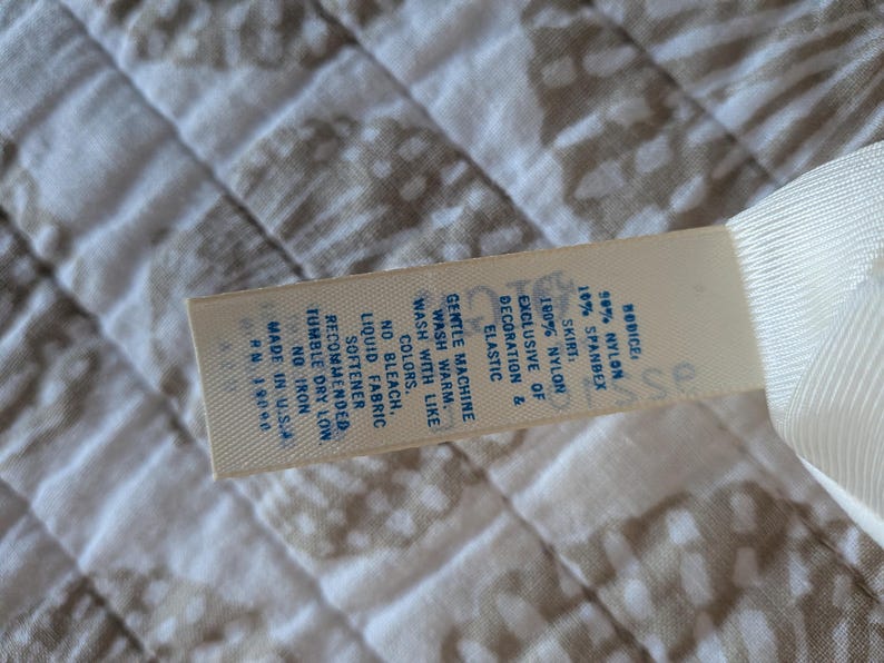 May include: A close-up of a tag with the text "RODICE" and fabric composition details: 50% nylon, 10% spandex, and 100% nylon skirt. The tag also includes washing instructions and "MADE IN U.S.A."