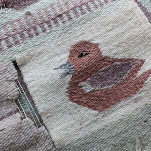 Pode incluir: Um close-up de uma tape&ccedil;aria tecida com um desenho de p&aacute;ssaro marrom. A tape&ccedil;aria &eacute; feita com uma variedade de cores, incluindo branco, verde e rosa.