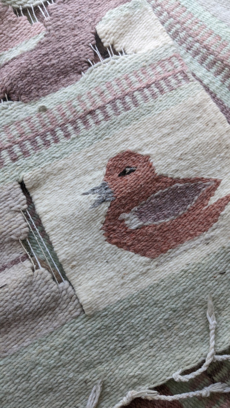 Pode incluir: Um close-up de uma tape&ccedil;aria tecida com um desenho de p&aacute;ssaro marrom. A tape&ccedil;aria &eacute; feita com uma variedade de cores, incluindo branco, verde e rosa.