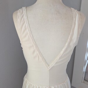 May include: Ivory-colored vintage nightgown with a V-neckline and delicate lace trim along the straps and neckline. The dress has a flowing, pleated skirt and is displayed on a mannequin. The fabric appears soft and lightweight.