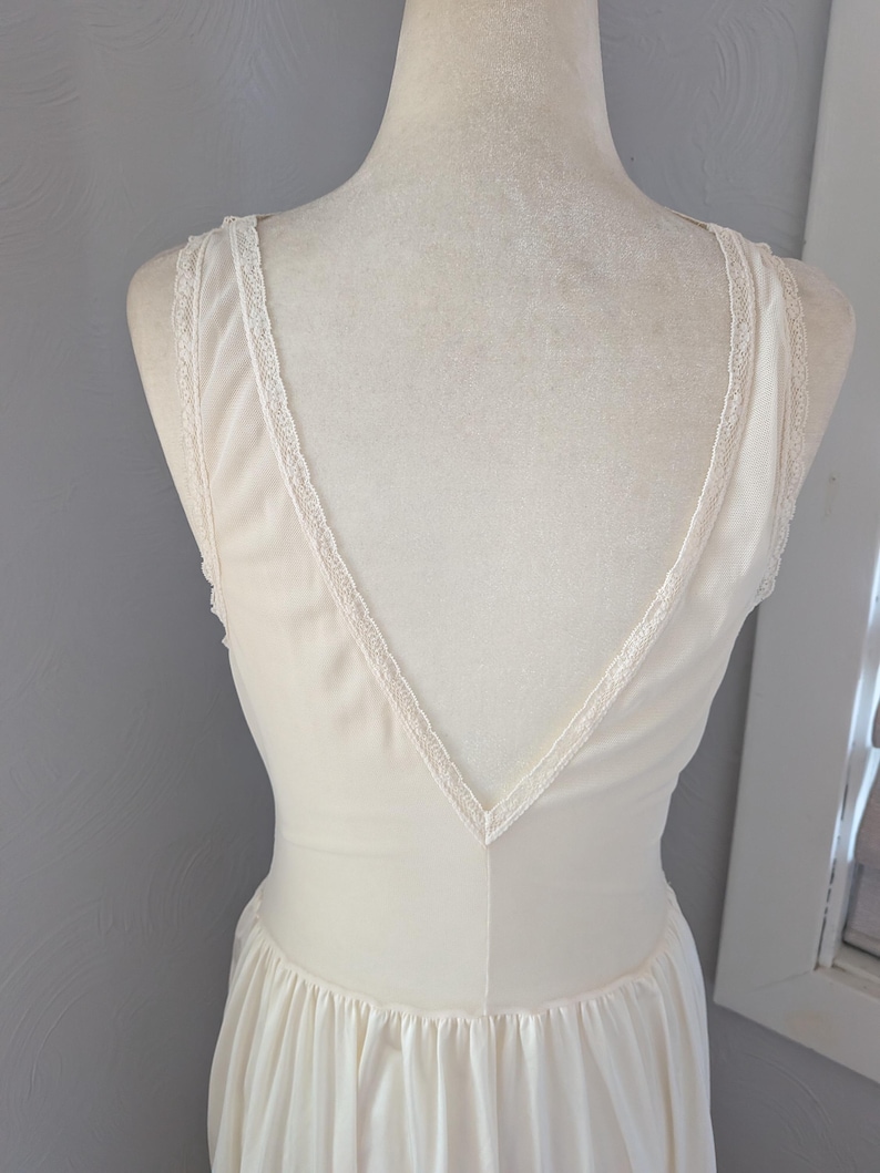 May include: Ivory-colored vintage nightgown with a V-neckline and delicate lace trim along the straps and neckline. The dress has a flowing, pleated skirt and is displayed on a mannequin. The fabric appears soft and lightweight.