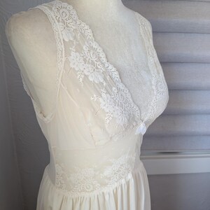 May include: Ivory-colored vintage slip dress with delicate lace detailing. The dress features a V-neckline and lace trim along the bodice and straps. The skirt is flowing and gathered at the waist, creating a classic silhouette.