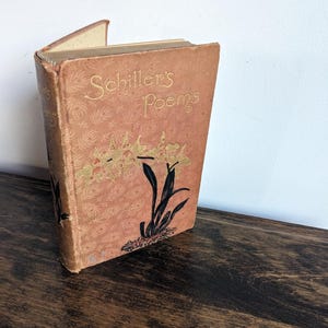 May include: A vintage book titled "Schiller's Poems" with a floral design on the cover. The book is bound in brown with gold lettering and a black and yellow floral illustration.