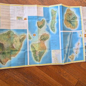 May include: Folded map of Hawaii, featuring detailed island illustrations in green and brown against a blue ocean backdrop. The map includes text labels and a small illustration of Diamond Head.