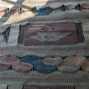 Pode incluir: Uma tape&ccedil;aria de parede tecida com um design geom&eacute;trico que apresenta uma &aacute;rvore, barcos e outras formas abstratas em tons de marrom, verde, azul e bege.