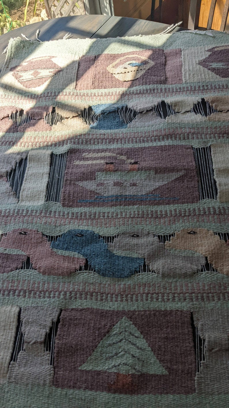 Pode incluir: Uma tape&ccedil;aria de parede tecida com um design geom&eacute;trico que apresenta uma &aacute;rvore, barcos e outras formas abstratas em tons de marrom, verde, azul e bege.