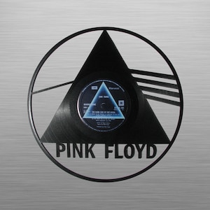 May include: A black vinyl record with a black triangle design and the text "PINK FLOYD" in white. The record is playing "The Dark Side of the Moon" by Pink Floyd.