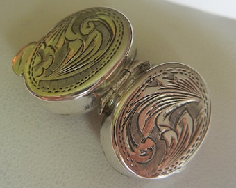 May include: A silver hinged locket with an intricate floral design engraved on both sides.
