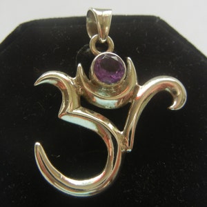 May include: Silver Om pendant with a purple amethyst gemstone. The pendant is intricately designed with a stylized Om symbol.