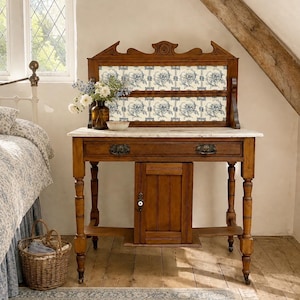 May include: A wooden washstand featuring a white marble top, a central cabinet with a white knob, and a decorative backboard with blue and white floral tiles. The piece stands on four turned legs with casters and includes a single drawer with two pulls.