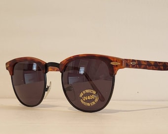 Op de afbeelding: Schildpadzonnebril met bruine glazen. De zonnebril heeft een gouden label met de tekst "100% UV Protection UV400 Protection Ultra Violet".