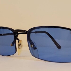 May include: A pair of black rimless sunglasses with blue lenses. The sunglasses have a thin metal frame and are in good condition.