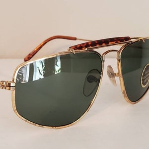 May include: Gold-tone aviator sunglasses with green lenses and a tortoise shell brow bar. The sunglasses have a metal frame and are in good condition.