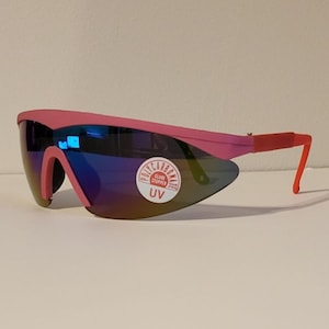 May include: Pink and red wraparound sunglasses with a blue mirrored lens. The sunglasses have a sticker that says "Polycarbonate Class 1 Stupper UV".