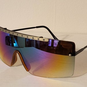 May include: A pair of large, wraparound sunglasses with a silver metal frame and iridescent lenses. The frame has a row of silver studs along the top.