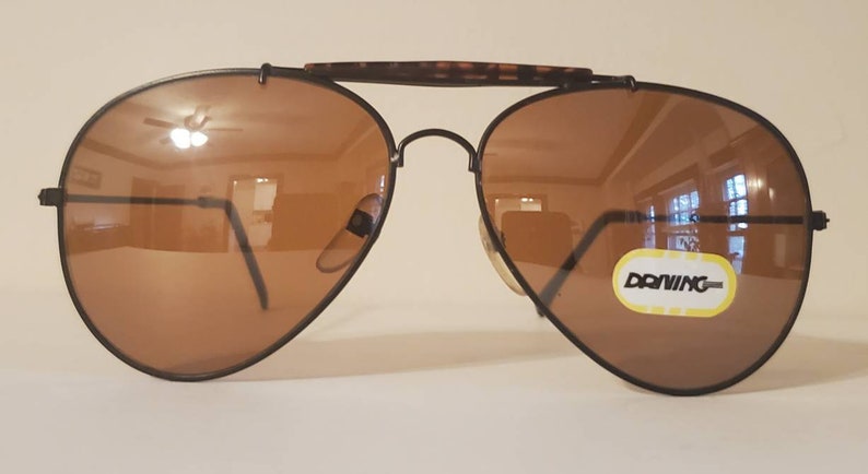 May include: Black aviator sunglasses with brown lenses and a brown tortoise shell frame. The sunglasses have a "Donwing" label on the right lens.