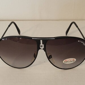 May include: Black Wrangler aviator sunglasses with gradient lenses. The sunglasses have a black frame with the Wrangler logo on the right lens and a white "W" on the bridge. A small UV protection sticker is on the right lens.