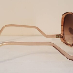 May include: Oversized, light brown sunglasses with gradient brown lenses. The frames and arms are a translucent light brown. The sunglasses are angled, showing the side view of the frames and lenses.