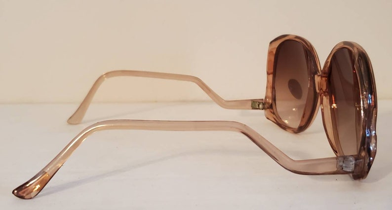 May include: Oversized, light brown sunglasses with gradient brown lenses. The frames and arms are a translucent light brown. The sunglasses are angled, showing the side view of the frames and lenses.