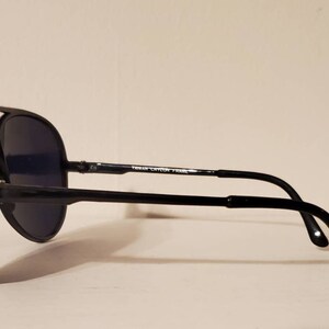 May include: Black aviator sunglasses with a black frame and dark lenses. The sunglasses have a metal bar on the bridge of the nose and the text "Taiwan Cycon Frame" is printed on the bar.