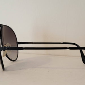 May include: Black aviator sunglasses with gradient lenses. The sunglasses feature a sleek, minimalist design with a black frame and temples. The lenses transition from dark to light, offering a stylish and functional accessory.